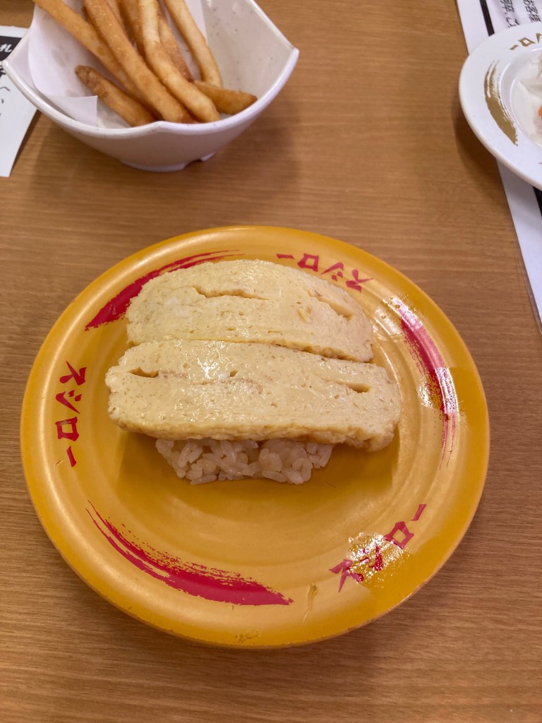 皿に盛られたたまご寿司とフライドポテトが写っている。たまご寿司は白ご飯の上に黄色の卵焼きが乗っている。背景にはテーブルの一部が見える。