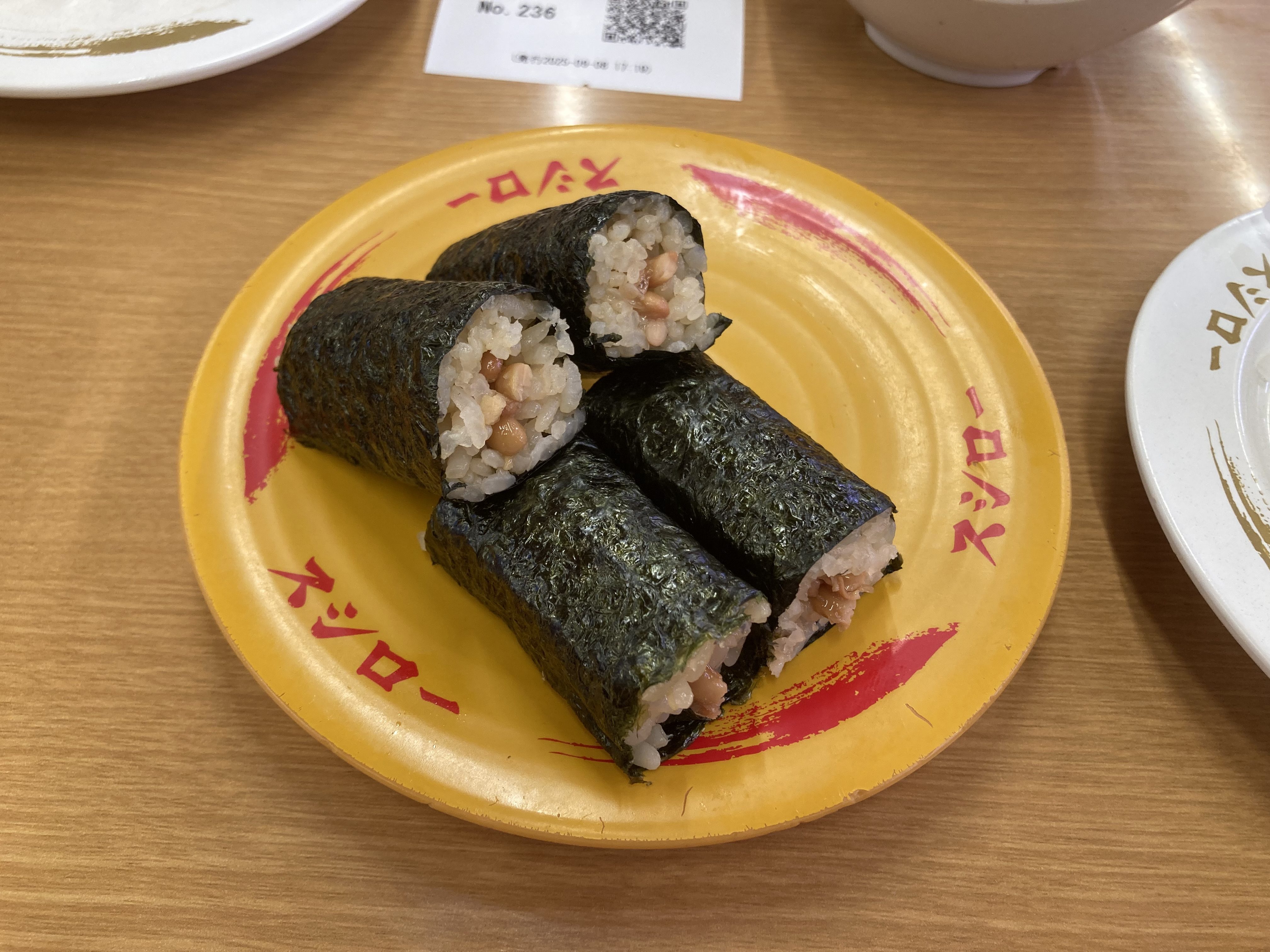 スシローの小粒納豆巻の皿に盛られた寿司の写真。海苔で巻かれた納豆の寿司が4個置かれている。